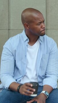 Vertical video: Raising cup while speaking, man wearing blue shirt and jeans, conversing off-camera