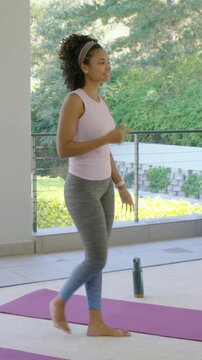 Vertical video: Doing squats, woman in tank leggings responding to cue on patio, mat and bottle