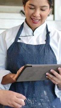 Vertical video: Positioning tablet, chef tapping recipe at prep counter showing chef coat and ovens
