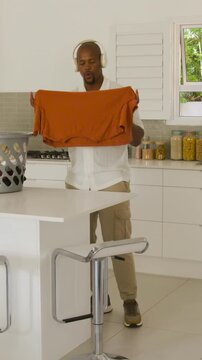 Vertical video: Picking up orange t-shirt from basket, man folding at island in kitchen, stacking