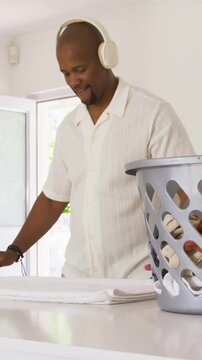 Vertical video: Reaching into gray basket, man white shirt folding towels at counter for neat stack