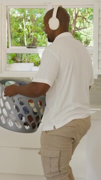 Vertical video: Walking man in white shirt with headset holding basket home opening to get laundry