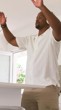 Vertical video: Dancing to music man with headphones, polo, shorts folding coat from bin in kitchen