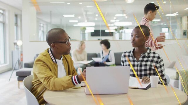 Man in mustard jacket pointing at laptop, woman writing notes, finalizing project plan in business
