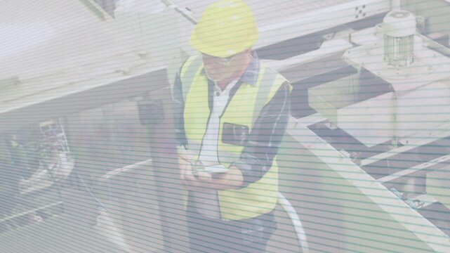 Senior tech tapping tablet on walkway, showing animated data for monitoring conveyors in factory