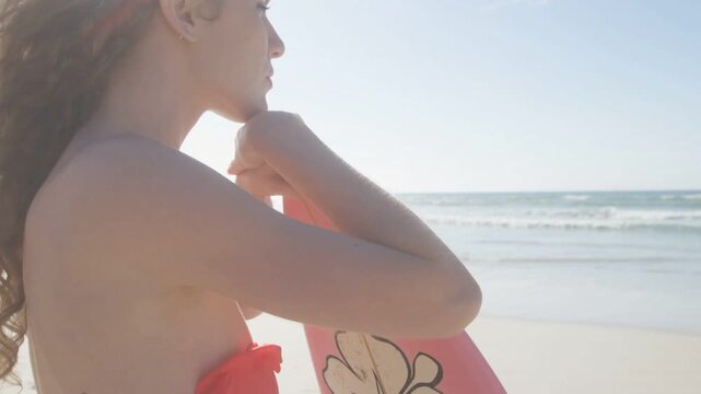 Female surfer holding pink board on beach, gazing at waves adjusting grip as health HUD animating