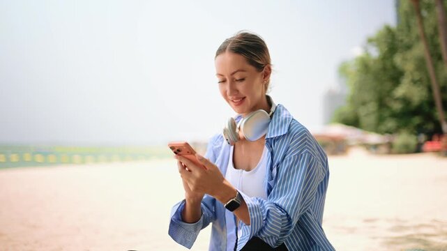 Active woman relaxing on the beach after workout, using laptop and listening to music, showcasing remote work, digital lifestyle, wellness