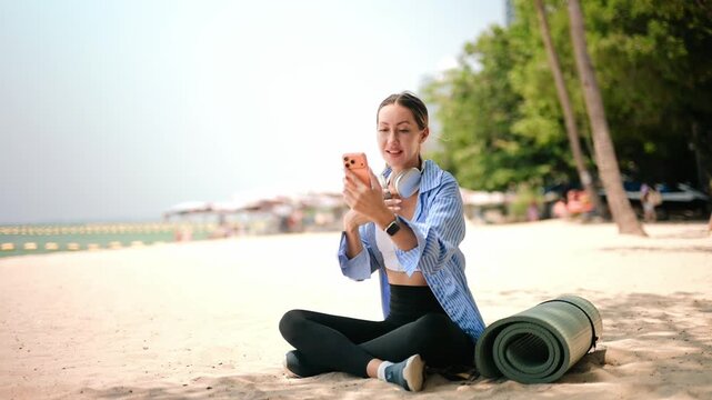 Active woman relaxing on the beach after workout, using laptop and listening to music, showcasing remote work, digital lifestyle, wellness