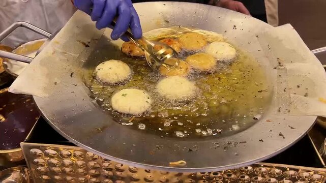 Aloo Tikki being fried in hot oil; a professional action shot of traditional Indian potato patties cooking on a large flat tawa for a street food market or wedding event.