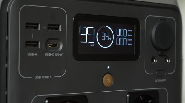 Close up of a man pressing power button on portable power station. Screen lights up showing system startup and energy supply activation.