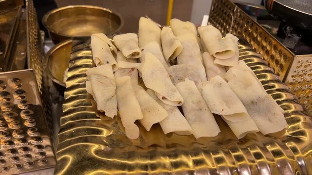 Handmade Patishapta (sweet rice-flour cr&ecirc;pes filled with coconut and jaggery) served at a grand Indian wedding banquet, showcasing artisanal dessert craftsmanship from West Bengal.
