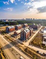 Obraz premium Aerial view showcases unfinished brick buildings amidst construction, roads, and surrounding urban landscape. A sunny sky dominates