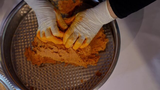 Close-up of gloved hands kneading kibbeh dough in a metal bowl, highlighting traditional Middle Eastern food preparation, texture, spices, and hygienic cooking process in kitchen.