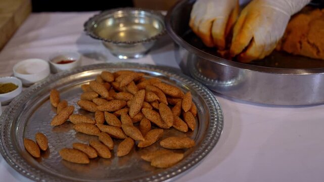 Close-up of raw shaped kibbeh arranged on a metal tray, ready for cooking, showcasing traditional Middle Eastern cuisine, bulgur texture, and batch food preparation process.