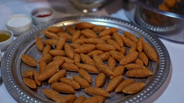 Close-up of raw shaped kibbeh arranged on a metal tray, ready for cooking, showcasing traditional Middle Eastern cuisine, bulgur texture, and batch food preparation process.
