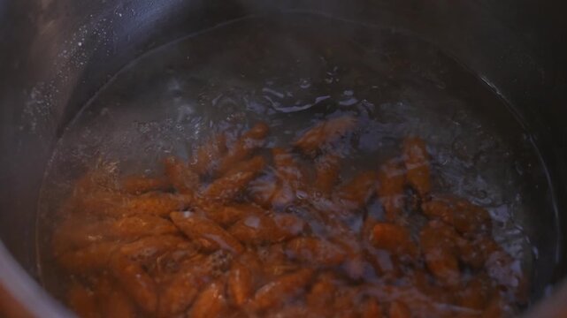 Close-up of kibbeh being dropped into boiling water, capturing dynamic cooking action, traditional preparation method, and authentic Middle Eastern cuisine in a professional kitchen setting.