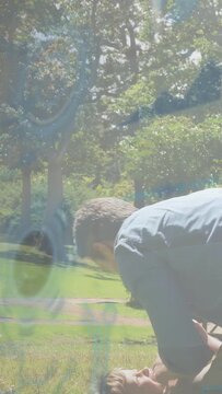 Vertical video: Dad entering, lifting child into sitting in park, reflection fading, aiding health