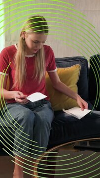 Vertical video: Woman unfolding mail on blue sofa reading finance mail while green overlay appears