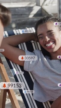 Vertical video: Reclining woman smiling and laughing on striped chair, reacting to floating likes