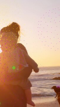 Vertical video: Mom holding baby walking shore sunset for health, cam pan fading flare dog trailing