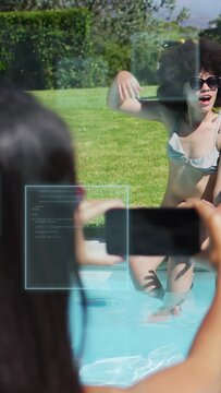 Vertical video: Friend tapping phone screen and filming woman pool edge, AR UI showing pose for ads