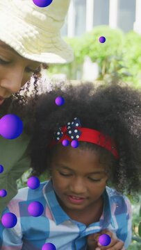Vertical video: Woman teaching child in garden, child inspecting plant, purple orbs drifting