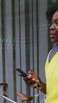 Vertical video: Woman tapping phone by slat wall, tech dots moving near buds, listening and smiling