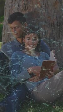 Vertical video: Pair sitting under tree, woman flipping book, sparking star overlay for education