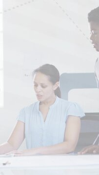Vertical video: Standing woman pointing at docs, guiding seated woman reading and typing for office