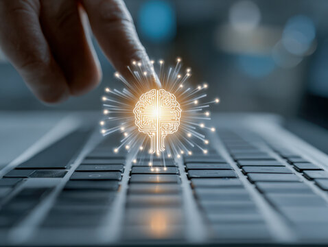 Human finger interacting with a futuristic digital brain icon symbolizing artificial intelligence and advanced technology on a laptop keyboard in a modern workplace
