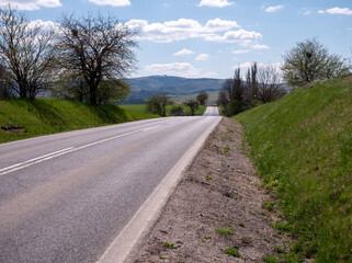 Fototapeta premium Gently rolling rural road winding over small hills, symbolizing travel, freedom, and a journey into the distance.