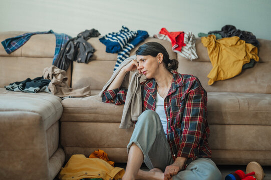 Tired woman sitting in living room with messy clothes on sofa