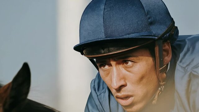 Close-up of a determined jockey in blue racing attire during a horse race. A jockey's intense focus is captured as they lean forward, urging their horse onward