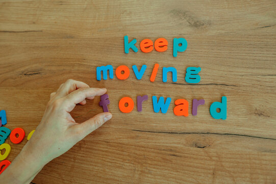 Hand arranging colorful letters to spell keep moving forward