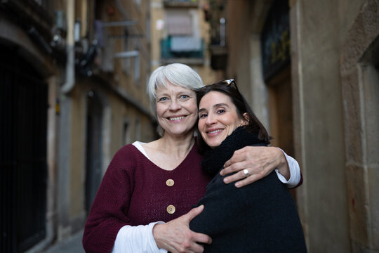 Joyful friends hugging and smiling while posing for a photo in a charming city alleyway