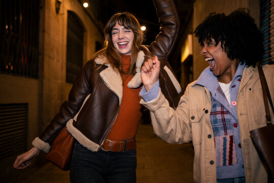 Happy friends dancing and laughing on a city street at night
