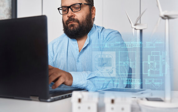 Architect working on laptop with futuristic hologram indoors