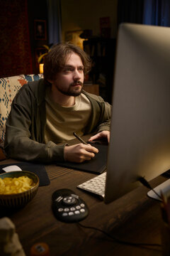 Freelancer drawing on graphic tablet in home office at night