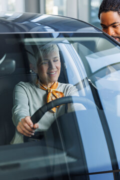 Salesperson with smiling customer examining car in showroom