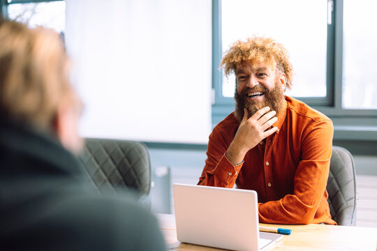 Happy mature businessman with hand on chin discussing with colleague