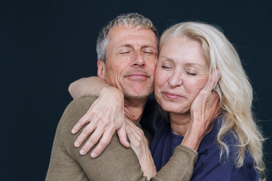 Smiling retired senior couple hugging with eyes closed against black background