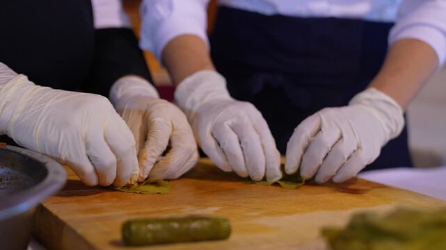 Close-up of a team preparing stuffed grape leaves with olive oil, showcasing traditional Turkish cuisine, teamwork in the kitchen, and handmade food preparation with fresh ingredients.