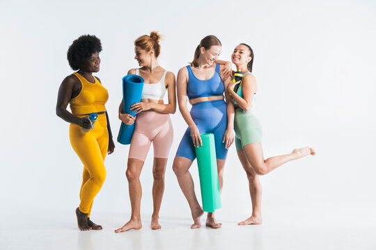 Happy friends standing with yoga mats and water bottles against white background