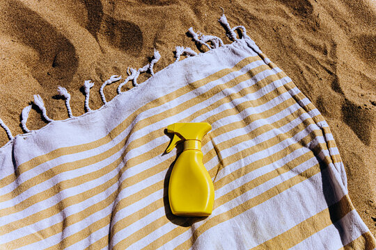 Yellow sunscreen spray bottle on a striped towel at the sandy beach
