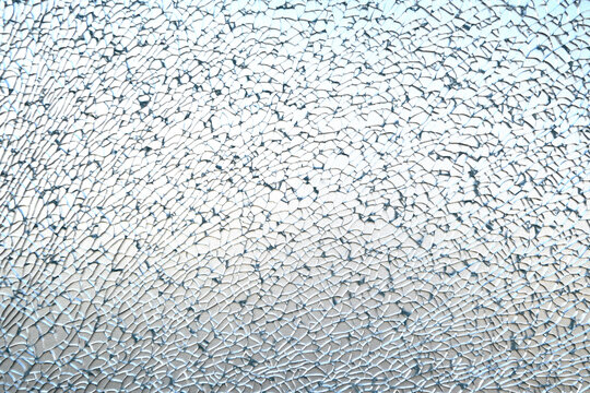 A close-up texture of completely shattered tempered glass, displaying an intricate web of tiny fragments.