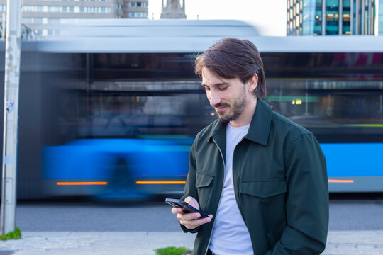 Commuter texting on smartphone in city with passing bus