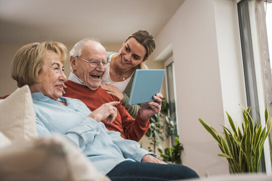 Smiling senior couple using tablet PC with home care giver in living room