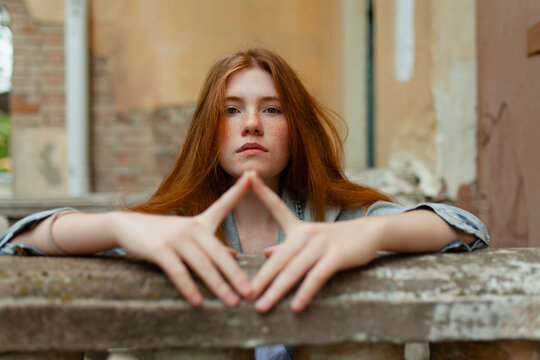 Portrait of teenage girl with red hair and freckles framing face with hands
