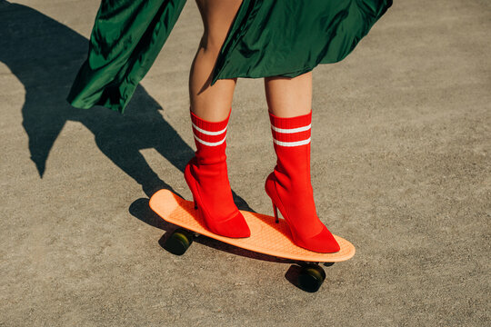 Legs in red high heel balancing on an orange skateboard
