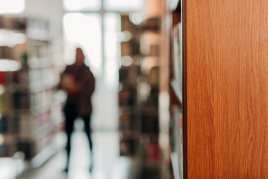 Blurred human figure behind wooden bookshelf in public library